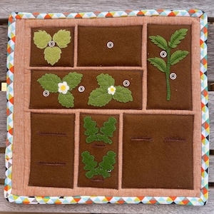May include: A brown felt board with nine squares, each containing a different felt appliqu&eacute; of a plant. The squares are outlined in a brown thread. The board is surrounded by a colorful trim.