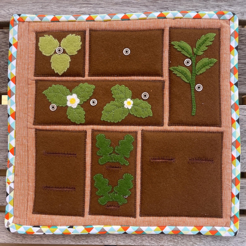 May include: A brown felt board with nine squares, each containing a different felt appliqu&eacute; of a plant. The squares are outlined in a brown thread. The board is surrounded by a colorful trim.