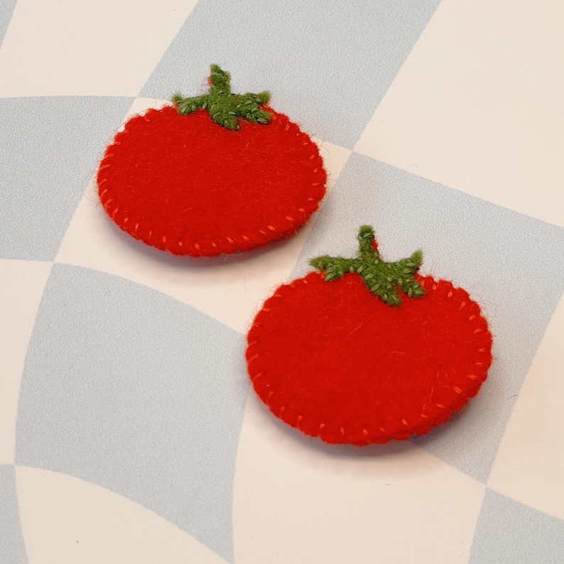 May include: Two red felt tomato shapes with green felt stems and leaves. The tomatoes are stitched around the edges.