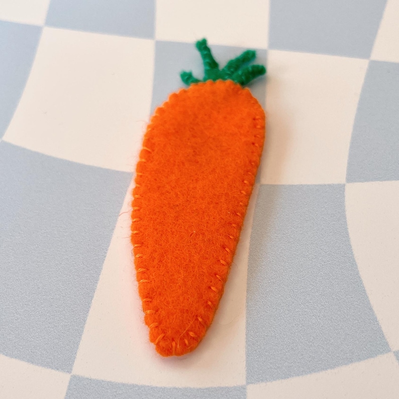 May include: A felt carrot with a green felt top. The carrot is orange and has a stitched outline.