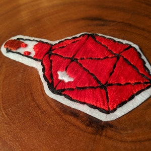 May include: Red embroidered patch of a potion bottle with a cork stopper. The bottle is shaped like a 20-sided die.
