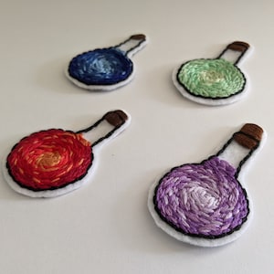 May include: Four embroidered felt potion bottles with cork stoppers. The potions are blue, green, red, and purple.