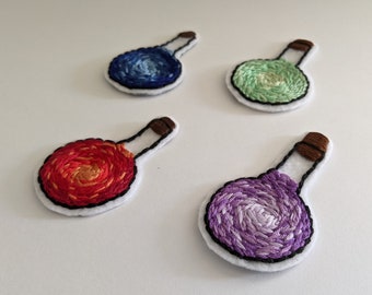 May include: Four embroidered felt potion bottles with cork stoppers. The potions are blue, green, red, and purple.