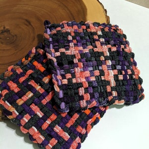 May include: Two woven pot holders in a black, purple, orange, and white checkered pattern.
