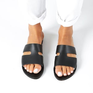 May include: A pair of black leather sandals with a double strap design. The sandals have a simple, minimalist style and are perfect for summer.