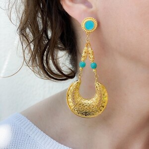 Op de afbeelding: Gouden oorbellen met een turquoise steen en een halve maan ontwerp.