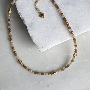 May include: A delicate gold necklace with brown and beige beads. The necklace has a small gold clasp.