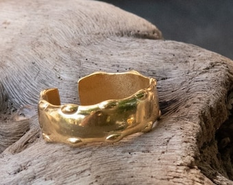 May include: A gold-toned ring with a textured, hammered finish. The ring is sitting on a piece of driftwood.