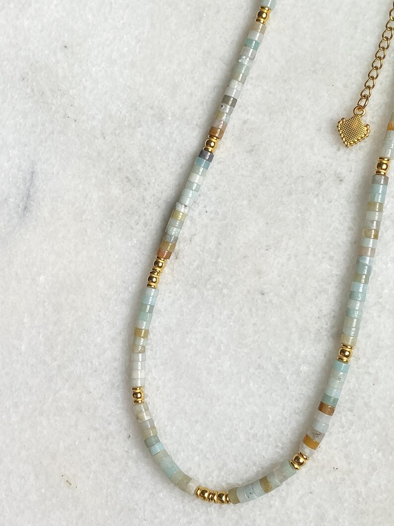 May include: A delicate gold chain necklace with a heart charm and a strand of light blue, white, and brown beads.