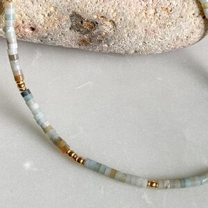 May include: A delicate necklace made with small, light blue, green, and beige beads interspersed with gold beads.