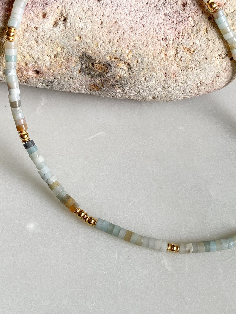 May include: A delicate necklace made with small, light blue, green, and beige beads interspersed with gold beads.