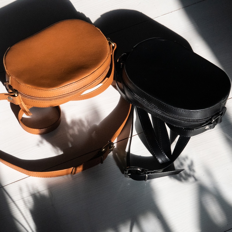 May include: Two round leather handbags, one brown and one black, with adjustable straps.