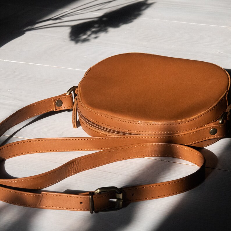 May include: A brown leather round crossbody bag with a zipper closure and a gold buckle on the strap.