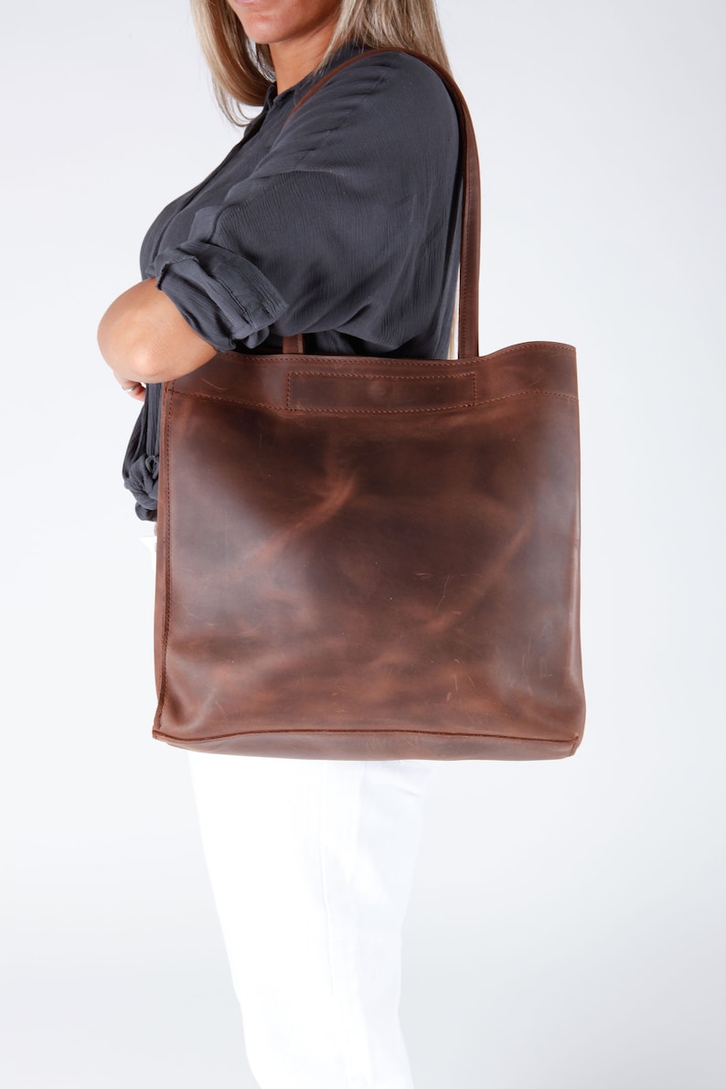 May include: A brown leather tote bag with a distressed finish. The bag has a single top handle and a wide opening.