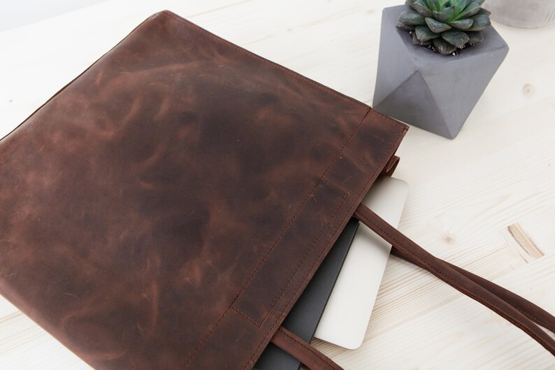May include: A brown leather tote bag with a laptop computer inside. The bag has two long straps and a zipper closure.