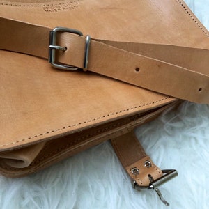 Puede incluir: Un bolso de cuero marr&oacute;n con una hebilla plateada y una correa. El bolso tiene un cierre de solapa y un borde cosido. La correa es ajustable y tiene una hebilla plateada. El bolso est&aacute; hecho de cuero genuino y est&aacute; hecho en Grecia.