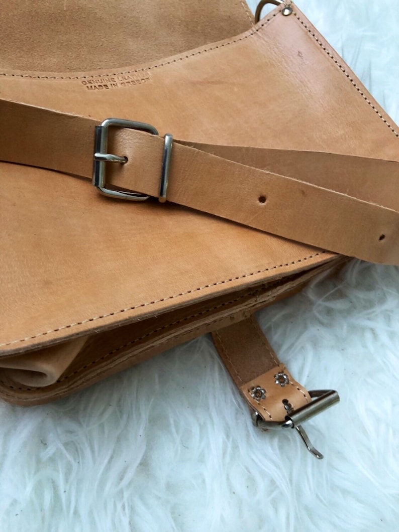 Puede incluir: Un bolso de cuero marr&oacute;n con una hebilla plateada y una correa. El bolso tiene un cierre de solapa y un borde cosido. La correa es ajustable y tiene una hebilla plateada. El bolso est&aacute; hecho de cuero genuino y est&aacute; hecho en Grecia.
