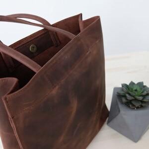 May include: A brown leather tote bag with a single snap closure. The bag has two handles and a large, open top.