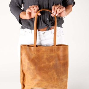 May include: A brown leather tote bag with a top handle. The bag has a distressed look and is made of a soft, supple leather.