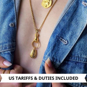 Peut inclure: Colliers dorés avec des pendentifs aux motifs complexes. L'un des colliers présente une main tenant un anneau avec un charm en forme de goutte. Un autre collier a un pendentif rond en forme de pièce. Les colliers sont présentés sur une veste en jean.