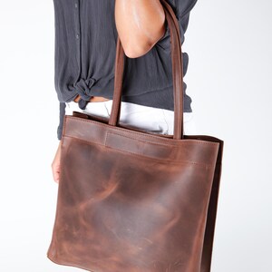 May include: A brown leather tote bag with a distressed finish. The bag has a wide, flat base and two long handles.