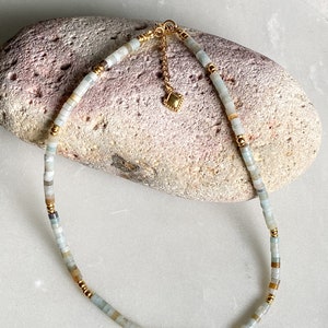 May include: A delicate gold chain necklace with a small gold charm and light blue and beige beads.