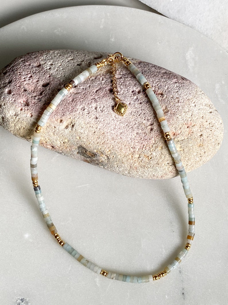 May include: A delicate gold chain necklace with a small gold charm and light blue and beige beads.