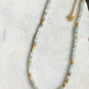 May include: A delicate gold chain necklace with a heart charm and a strand of light blue, white, and brown beads.
