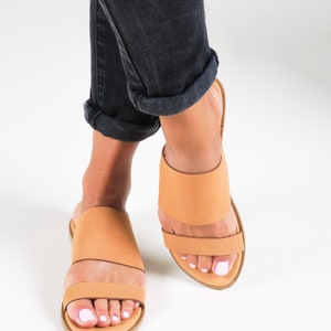 May include: A pair of tan leather slide sandals with a double strap design. The sandals have a simple, minimalist style and are perfect for warm weather.