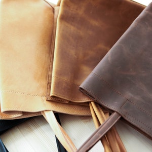 May include: Four leather tote bags in different colors: black, tan, brown, and dark brown. The bags are made of a distressed leather and have a simple design with a single handle.