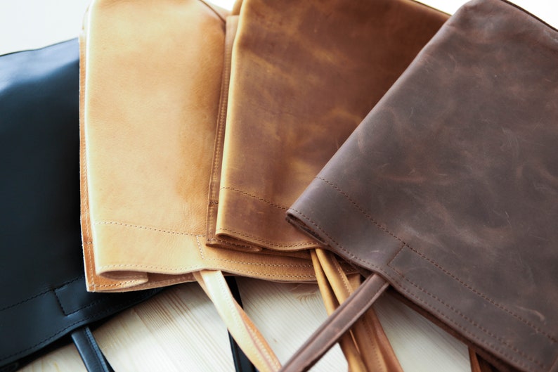 May include: Four leather tote bags in different colors: black, tan, brown, and dark brown. The bags are made of a distressed leather and have a simple design with a single handle.