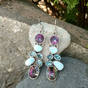 May include: A pair of dangle earrings with a silver setting and multiple gemstones. The earrings feature a large iridescent purple gemstone at the top, followed by a smaller turquoise gemstone, and then a cluster of smaller blue and turquoise gemstones.
