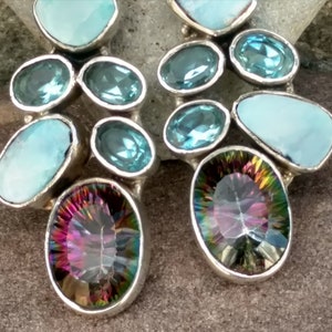 May include: A pair of silver earrings with a cluster of blue and iridescent gemstones. The earrings feature a mix of round and oval-shaped stones.