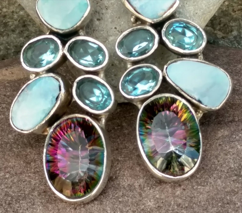 May include: A pair of silver earrings with a cluster of blue and iridescent gemstones. The earrings feature a mix of round and oval-shaped stones.