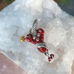 K&ouml;nnte beinhalten: Ein roter Hummer-Anh&auml;nger mit dem Wort "MAINE" in silbernen Buchstaben. Der Hummer hat herzf&ouml;rmige Akzente und eine goldfarbene Kugel. Der Anh&auml;nger h&auml;ngt an einer silberfarbenen &Ouml;se.