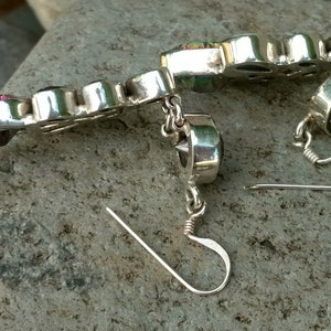 May include: A pair of silver earrings with iridescent gemstones. The earrings have a dangle design with a small chain and a hook closure.