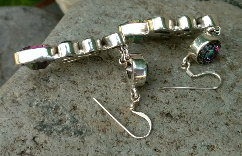 May include: A pair of silver earrings with iridescent gemstones. The earrings have a dangle design with a small chain and a hook closure.