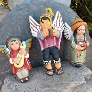 May include: Three ceramic angel figurines with wings, each playing a different musical instrument. The angel on the left is playing a lute, the angel in the middle is playing a tambourine, and the angel on the right is playing a drum.
