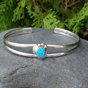 May include: A silver bracelet with a double band and a blue opal stone set in a silver heart-shaped bezel.