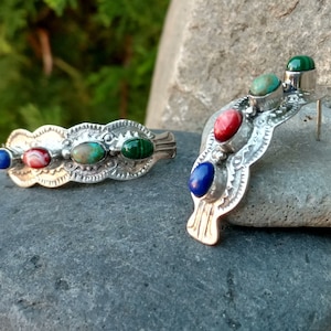 May include: A pair of silver earrings with a curved design and colorful stones. The stones are blue, red, green, and turquoise.