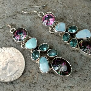 May include: A pair of dangle earrings with a silver setting. The earrings feature a large iridescent gemstone, turquoise stones, and smaller blue gemstones.