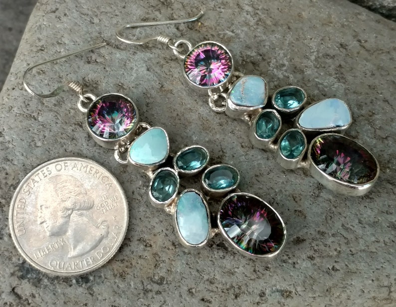 May include: A pair of dangle earrings with a silver setting. The earrings feature a large iridescent gemstone, turquoise stones, and smaller blue gemstones.