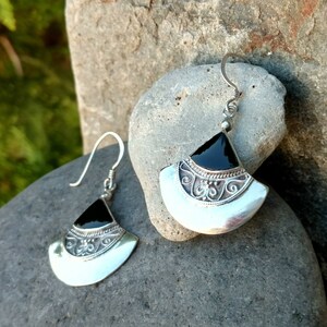 May include: A pair of silver earrings with black onyx stones. The earrings are shaped like a fan and have intricate silver detailing.