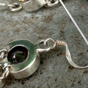 May include: A pair of silver earrings with a dark green gemstone set in a silver oval. The earrings have a lever back closure.