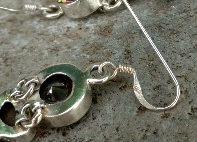 May include: A pair of silver earrings with a dark green gemstone set in a silver oval. The earrings have a lever back closure.