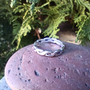 May include: A silver ring with a braided design. The ring is sitting on a brown rock.