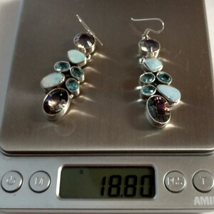 May include: A pair of silver dangle earrings with a cluster of blue and purple gemstones. The earrings are on a digital scale that reads 18.80.