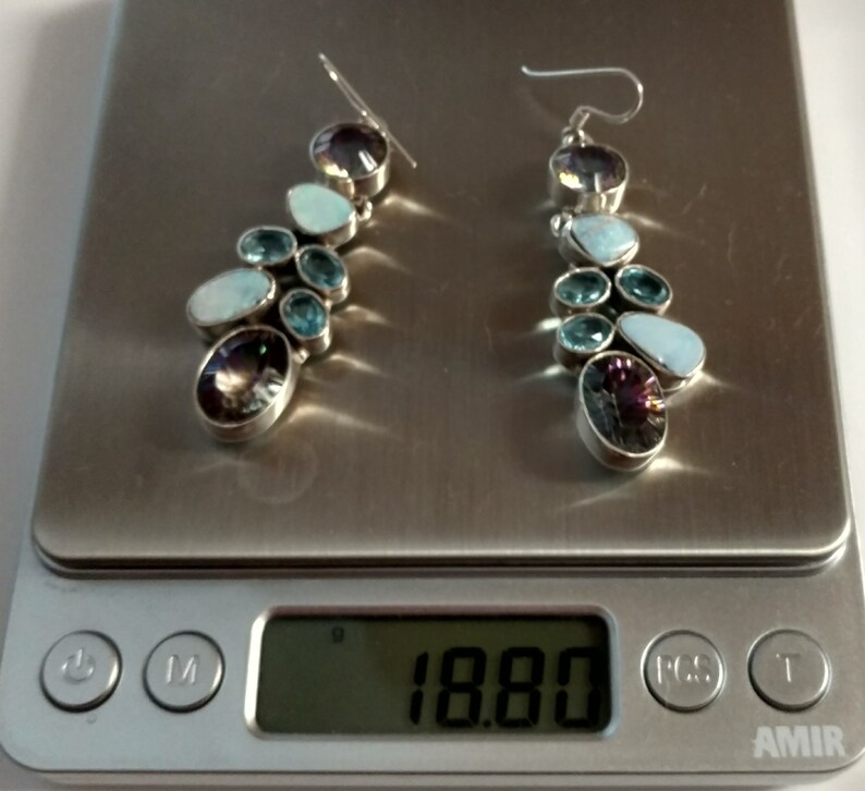 May include: A pair of silver dangle earrings with a cluster of blue and purple gemstones. The earrings are on a digital scale that reads 18.80.