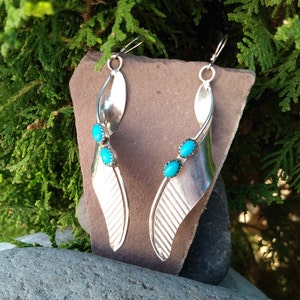 May include: A pair of silver dangle earrings with turquoise stones. The earrings are shaped like a leaf and have a textured design.