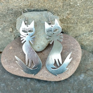 May include: A pair of silver cat-shaped earrings. The cats have large eyes and a simple, stylized design.